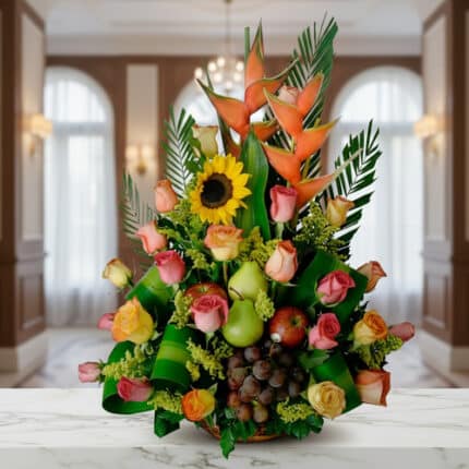 Arreglo floral con rosas de colores, girasol, heliconias y frutas como uvas, peras y manzanas sobre una mesa de mármol en interior elegante