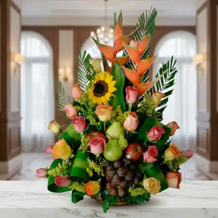 Arreglo floral con rosas de colores, girasol, heliconias y frutas como uvas, peras y manzanas sobre una mesa de mármol en interior elegante