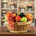 Canasta de mimbre llena de frutas variadas como uvas, manzanas, peras, duraznos y ciruelas sobre una mesa de madera con fondo de estantería decorada con flores y luces