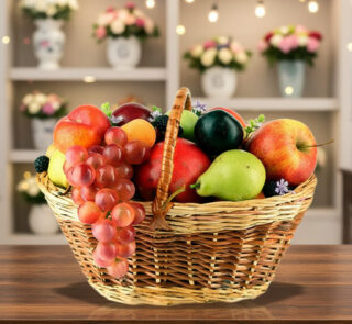 Canasta de mimbre llena de frutas variadas como uvas, manzanas, peras, duraznos y ciruelas sobre una mesa de madera con fondo de estantería decorada con flores y luces