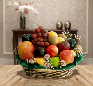 Canasta tejida con variedad de frutas frescas como manzanas, uvas, mangos y cítricos sobre una mesa de madera, con fondo de sala elegante desenfocado