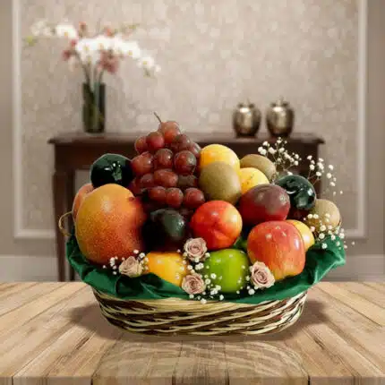 Canasta tejida con variedad de frutas frescas como manzanas, uvas, mangos y cítricos sobre una mesa de madera, con fondo de sala elegante desenfocado