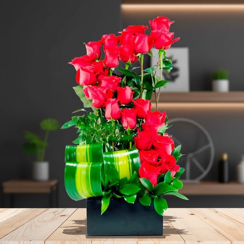 Arreglo moderno de rosas rojas en base negra Arreglo floral con rosas rojas frescas en maceta rectangular negra sobre mesa de madera, con hojas verdes decorativas y fondo de sala moderna desenfocado