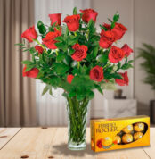Arreglo de rosas rojas en jarrón de cristal junto a una caja de chocolates Ferrero Rocher sobre una mesa de madera en sala iluminada