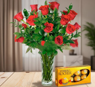 Arreglo de rosas rojas en jarrón de cristal junto a una caja de chocolates Ferrero Rocher sobre una mesa de madera en sala iluminada