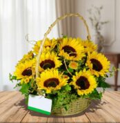 Arreglo floral de girasoles amarillos en canasta trenzada con asa, sobre mesa de madera en interior desenfocado