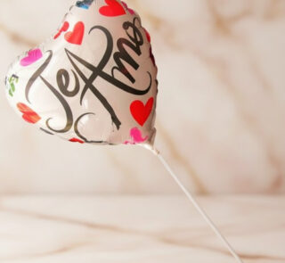 Globo metálico en forma de corazón con la frase Te Amo y varios corazones de colores sobre fondo desenfocado beige