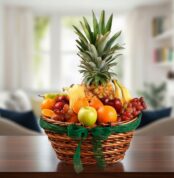 Canasta de mimbre con piña, uvas, manzanas, naranjas, plátanos y otras frutas variadas sobre una mesa de madera en sala desenfocada