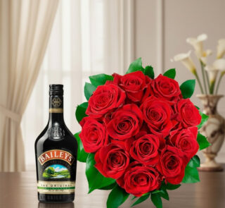 Botella de licor Baileys junto a un ramo de rosas rojas con hojas verdes sobre una mesa de madera, con cortinas claras y florero desenfocado al fondo