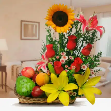 Canasta de mimbre con frutas variadas y arreglo floral con girasol, rosas rojas, lirios amarillos y rosas, sobre una mesa en una sala de estar desenfocada