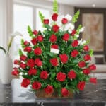 Arreglo grande de rosas rojas con follaje verde en base rectangular de madera sobre mesa de mármol negra en sala moderna