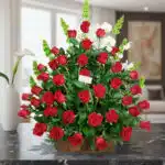 Arreglo grande de rosas rojas con follaje verde en base rectangular de madera sobre mesa de mármol negra en sala moderna