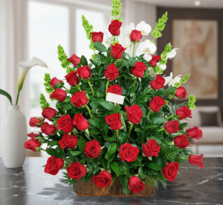 Arreglo grande de rosas rojas con follaje verde en base rectangular de madera sobre mesa de mármol negra en sala moderna