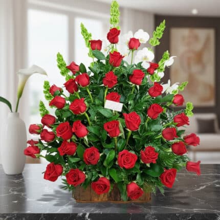 Arreglo grande de rosas rojas con follaje verde en base rectangular de madera sobre mesa de mármol negra en sala moderna