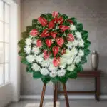 Corona floral redonda con anturios rojos y flores blancas sobre caballete de madera en interior