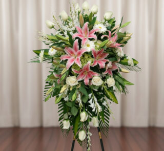 Arreglo floral alto sobre caballete con lirios rosas, rosas blancas y follaje verde frente a una cortina beige