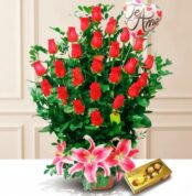 Arreglo floral de rosas rojas con lirios rosas al frente, globo con mensaje de amor y caja de chocolates Ferrero Rocher sobre fondo claro