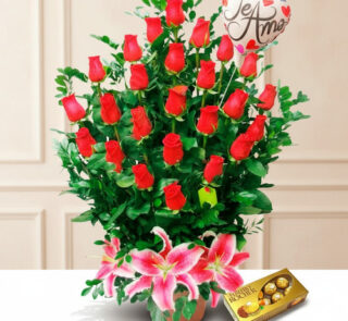 Arreglo floral de rosas rojas con lirios rosas al frente, globo con mensaje de amor y caja de chocolates Ferrero Rocher sobre fondo claro