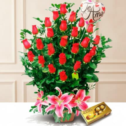 Arreglo floral de rosas rojas con lirios rosas al frente, globo con mensaje de amor y caja de chocolates Ferrero Rocher sobre fondo claro