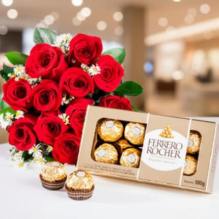 Ramo de rosas rojas con flores blancas pequeñas junto a una caja abierta de chocolates Ferrero Rocher sobre fondo desenfocado