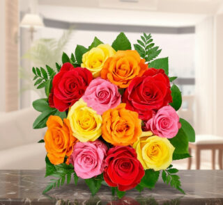 Arreglo floral con rosas rojas, rosas, amarillas y naranjas sobre una mesa de mármol en una sala iluminada