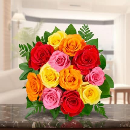 Arreglo floral con rosas rojas, rosas, amarillas y naranjas sobre una mesa de mármol en una sala iluminada