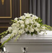 Arreglo de flores blancas con lirios y claveles sobre un ataúd blanco en una sala funeraria elegante