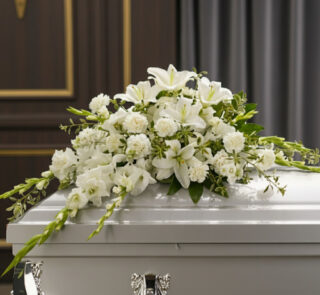 Arreglo de flores blancas con lirios y claveles sobre un ataúd blanco en una sala funeraria elegante