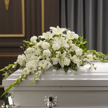 Arreglo de flores blancas con lirios y claveles sobre un ataúd blanco en una sala funeraria elegante