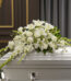 Arreglo de flores blancas con lirios y claveles sobre un ataúd blanco en una sala funeraria elegante