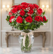 Arreglo de rosas rojas con paniculata blanca en jarrón de cristal con lazo beige sobre mesa de mármol