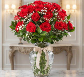 Arreglo de rosas rojas con paniculata blanca en jarrón de cristal con lazo beige sobre mesa de mármol