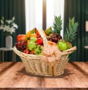 canasta de mimbre con lazo decorativo llena de frutas variadas como piñas, uvas, manzanas, peras y plátanos sobre mesa de madera con fondo de sala desenfocado