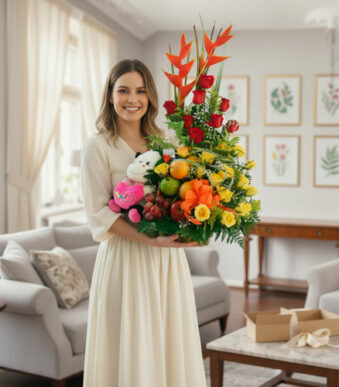 Mujer joven de vestido claro sosteniendo un gran arreglo de flores y frutas con peluche en una sala de estar luminosa