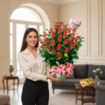 Mujer joven sonriendo sostiene un gran arreglo de rosas rojas y lirios rosados con un globo en forma de corazón que dice Te Amo en una sala elegante