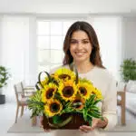Mujer sonriente con suéter beige sostiene una canasta de mimbre con girasoles amarillos y follaje verde en una sala de estar moderna y luminosa