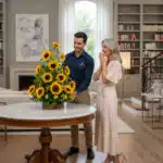 Hombre entregando un gran arreglo de girasoles a una mujer emocionada en una sala de estar elegante con mesa redonda de mármol