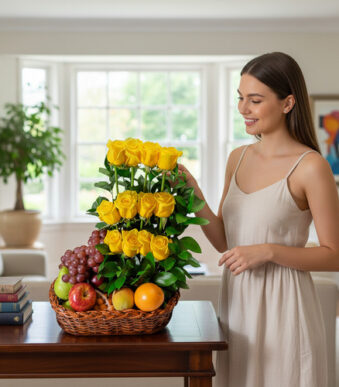 Mujer joven junto a una canasta de mimbre con rosas amarillas en varios niveles y frutas frescas sobre una mesa de madera en sala iluminada