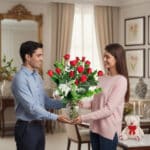 Hombre entregando a una mujer un ramo de rosas rojas en un florero de cristal dentro de una sala elegante, con peluche blanco y velas al fondo
