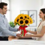 Hombre joven entrega a mujer un ramo de girasoles amarillos en jarrón de cristal con lazo rojo en interior luminoso