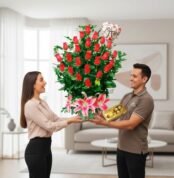 Hombre entrega a mujer un gran arreglo de rosas rojas con lirios rosas, globo de te amo y caja de chocolates en una sala de estar luminosa