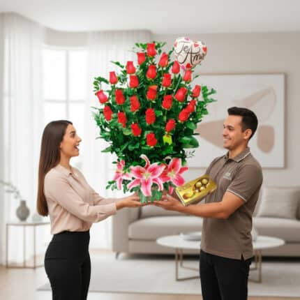 Hombre entrega a mujer un gran arreglo de rosas rojas con lirios rosas, globo de te amo y caja de chocolates en una sala de estar luminosa