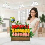 Mujer sonriente junto a un arreglo de rosas rojas, amarillas y rosas en base de madera con globo de Happy Birthday en una sala luminosa