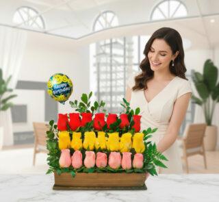 Mujer sonriente junto a un arreglo de rosas rojas, amarillas y rosas en base de madera con globo de Happy Birthday en una sala luminosa