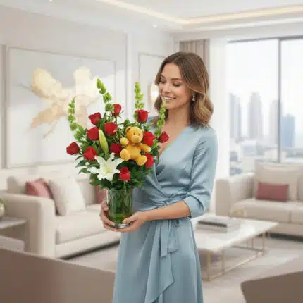 Mujer joven con vestido azul sosteniendo un ramo de rosas rojas, lirios blancos y peluche en un florero de vidrio dentro de una sala de estar moderna y luminosa