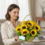 Mujer joven con blusa beige sosteniendo una canasta de mimbre llena de girasoles amarillos con tarjeta en una sala de estar luminosa
