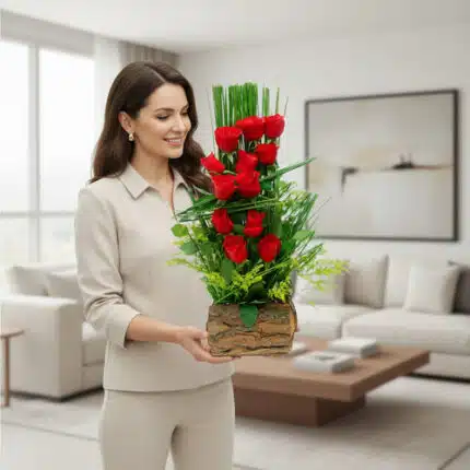 Mujer joven con traje beige sosteniendo un arreglo vertical de rosas rojas y follaje verde en maceta de aspecto rústico dentro de una sala de estar luminosa y moderna