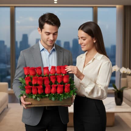 Hombre y mujer jóvenes sosteniendo juntos un arreglo rectangular de rosas rojas en tres niveles dentro de un departamento moderno con ventanales a la ciudad