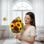 Mujer joven de cabello castaño sostiene un ramo de girasoles amarillos y rosas rojas envuelto en papel kraft, de pie en una sala de estar luminosa con ventanal al fondo