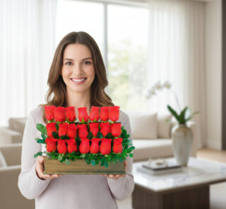 Mujer joven sonriente sostiene un arreglo rectangular de rosas rojas con follaje verde en una sala de estar luminosa y moderna